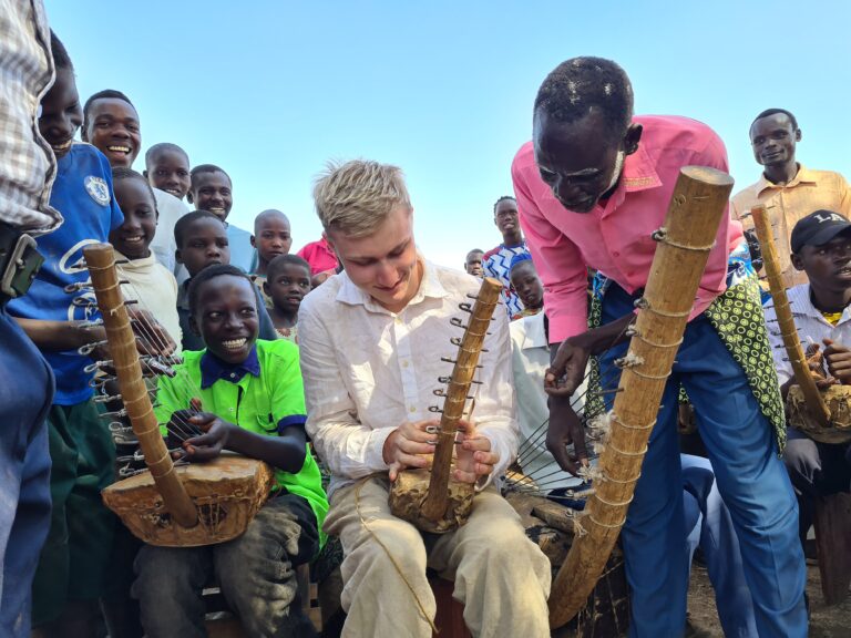 Guest at Alakara Guest House learning to play local instrument adungu during a traditional music workshop in Kobulin, Karamoja, Uganda